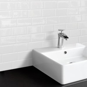 Puede incluir: Un lavabo de baño de cerámica blanca con un grifo cromado. El lavabo está colocado contra una pared de azulejos blancos tipo metro.
