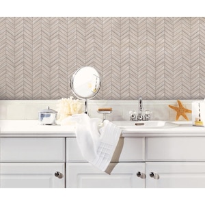 May include: White bathroom vanity with a white ceramic sink and chrome faucet. The backsplash is a herringbone pattern of light brown and gray tiles. A white towel is draped over the counter, and a round mirror is hanging on the wall.