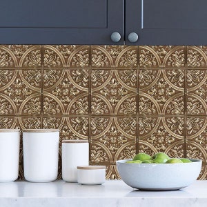May include: Gold metallic tile backsplash with a decorative embossed pattern. The backsplash is installed in a kitchen behind a countertop with white ceramic containers and a white bowl filled with green apples.