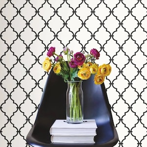 May include: A black and white geometric patterned wallpaper with a black chair and a vase of yellow and pink flowers.