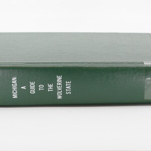 May include: A green hardcover book titled "Michigan: A Guide to the Wolverine State." The book has white text and a sticker with the numbers "917.74 Michigan 1941." The book is on a white background.