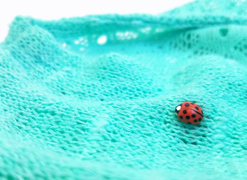 Pictured is a realistic, life-size ladybug pin on a sheer mint blue sweater