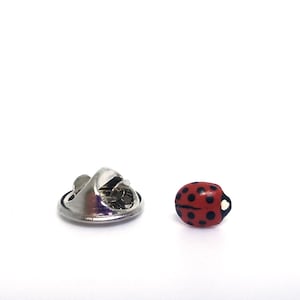 Pictured is a realistic red ladybug pin on a solid white background.