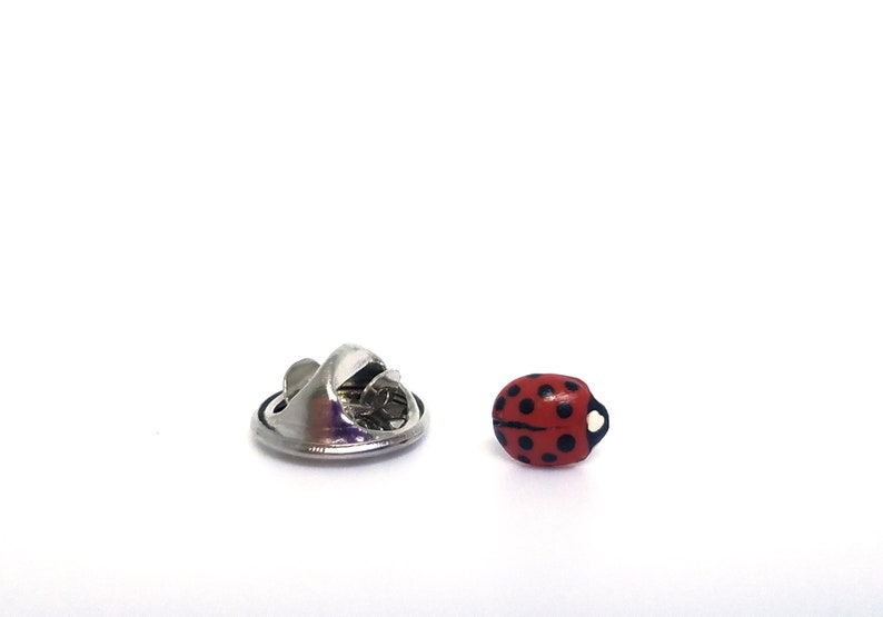 Pictured is a realistic red ladybug pin on a solid white background.