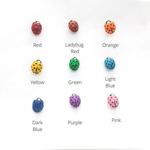 May include: Nine ladybug figurines in different colors: red, ladybug red, orange, yellow, green, light blue, dark blue, purple, and pink. Each ladybug has black spots.