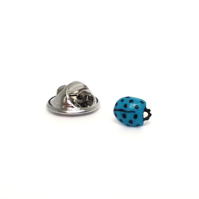 Pictured is a light blue ladybug pin on a solid white background.