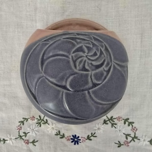 May include: A grey ceramic wall pocket with a spiral design. The top rim is light pink, and it has a curved handle. This wall pocket is likely for displaying flowers or small plants. The measurements are in centimetres.