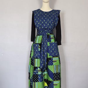 May include: A vintage patchwork dress on a mannequin. The dress features a blue floral bodice, black long sleeves, and a patchwork skirt with green, blue, and black geometric patterns. A dark blue headband completes the look.