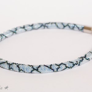 Peut inclure: Un collier délicat en perles bleues et noires avec un fermoir argenté. Les perles sont disposées en un motif géométrique.