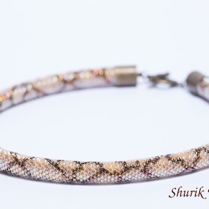 Peut inclure: Un collier de perles blanc et brun avec un motif en forme de serpent. Le collier a un fermoir argenté.