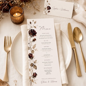 May include: A tall, rectangular wedding menu card and a matching folded place card featuring dark red rose illustrations. The menu lists courses including appetizer, salad, entree, dessert, and beverages, ending with the names Olivia & Marcus.