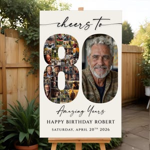 以下が含まれることがあります： イーゼルに立てられたクリーム色の誕生日の看板。「Cheers to 80 Amazing Years」と書かれており、「Robert」という名前と「Saturday, April 20th 2026」という日付が記載されています。数字の80は男性の小さな写真で埋められています。