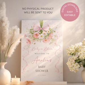 May include: A baby shower welcome sign with a floral bouquet and pink ribbon design. The sign reads "Baby in Bloom" and welcomes guests to Amelia's baby shower. The sign is a digital download.