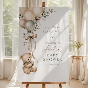 Może przedstawiać: Prostokątny znak powitalny na baby shower z akwarelową ilustracją pluszowego misia trzymającego pęk beżowych i szałwiowo-zielonych balonów ze wstążką. Tekst brzmi: we can BEARLY WAIT WELCOME TO Amelia's BABY SHOWER SAT, SEPT 19TH.
