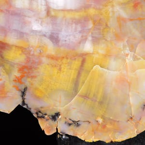 May include: Close-up of a polished, colorful stone with a natural, layered pattern. The stone features a mix of yellow, orange, white, and red hues, with dark black accents. The surface has a smooth, glossy appearance.