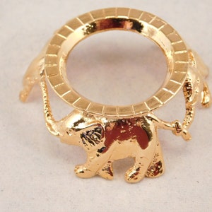 May include: Gold metal decorative stand with a round top and three elephant legs. The stand is designed to hold a small object, such as a crystal ball.