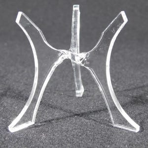 Może przedstawiać: Przezroczysty stojak wystawowy z tworzywa sztucznego z trzema nogami, zaprojektowany do trzymania okrągłego przedmiotu.