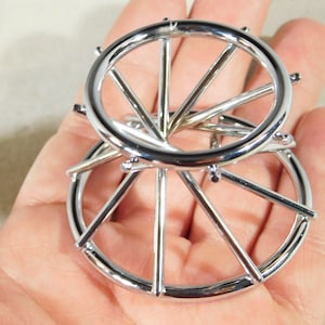 May include: A polished, chrome metal puzzle with two interconnected circular wheel-shaped components. The puzzle has spokes extending from the centre, forming a complex and captivating design. The image highlights the puzzle's intricate details and reflective surface.