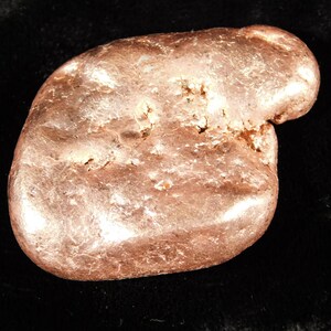 May include: A natural, irregularly shaped gold nugget with a textured surface. The nugget has a warm, metallic color and appears to be solid. The overall shape is rounded with some protrusions.