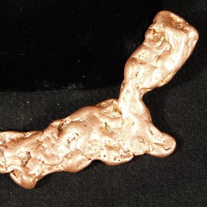 May include: A natural copper nugget with a rough, textured surface and a warm, reddish-brown color. The nugget has an irregular, organic shape, and is displayed against a dark background.