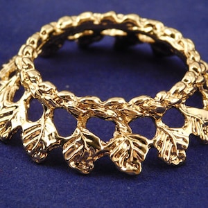May include: Gold-toned metal ring with a decorative design of leaves. The ring is open and has a circular shape.