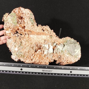 May include: A raw copper mineral specimen with a rough, crystalline texture and patches of green oxidation. The specimen is positioned above a Westcott ruler, showing a length of approximately 11 inches across its widest horizontal section.