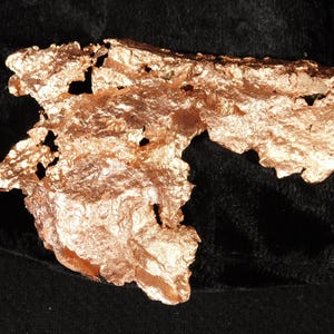Peut inclure: Un spécimen de cuivre métallique brut présentant une forme irrégulière et dentelée avec une surface texturée et réfléchissante. La pièce affiche une teinte brun-rougeâtre chaude avec des crevasses profondes et des ouvertures poreuses.