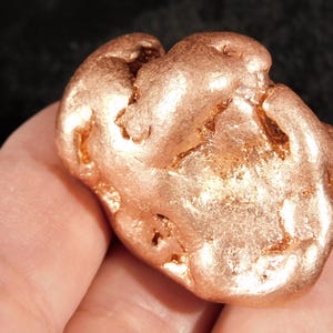 Könnte beinhalten: Ein roher, metallischer Kupfernugget mit einer glänzenden, rotbraunen Oberfläche. Das Objekt weist eine unregelmäßige, klumpige und organische Form mit tiefen Spalten sowie glatten, abgerundeten Vorsprüngen über die gesamte äußere Textur auf.