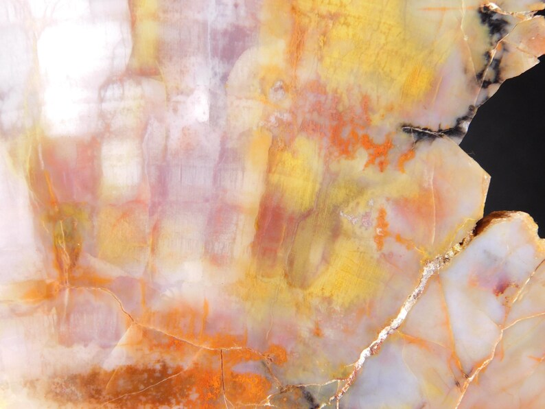 May include: Abstract close-up of a polished stone surface. The stone features a blend of colors, including yellow, orange, white, and hints of purple. The surface has a natural, textured appearance with visible veins and patterns.