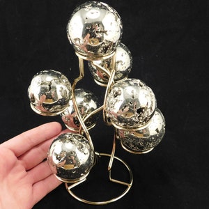 May include: A gold metal stand with six shiny, silver, pyrite spheres. The spheres are arranged in a tree-like formation.