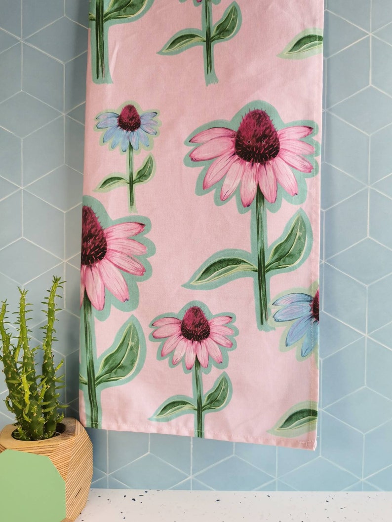 May include: Pink kitchen towel with a floral pattern of purple and pink coneflowers with green leaves.