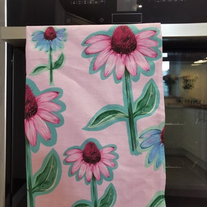 May include: Pink kitchen towel with a floral pattern of pink and purple flowers with green leaves. The flowers are outlined in teal.
