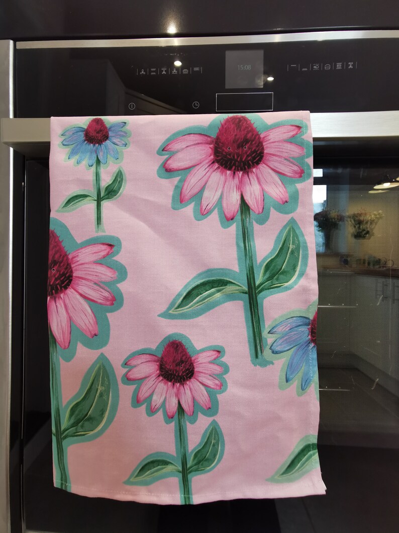 May include: Pink kitchen towel with a floral pattern of pink and purple flowers with green leaves. The flowers are outlined in teal.