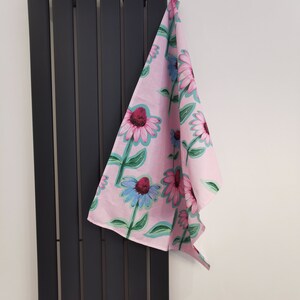May include: A pink tea towel with a floral pattern of pink, blue, and green flowers. The towel is hanging on a black radiator.