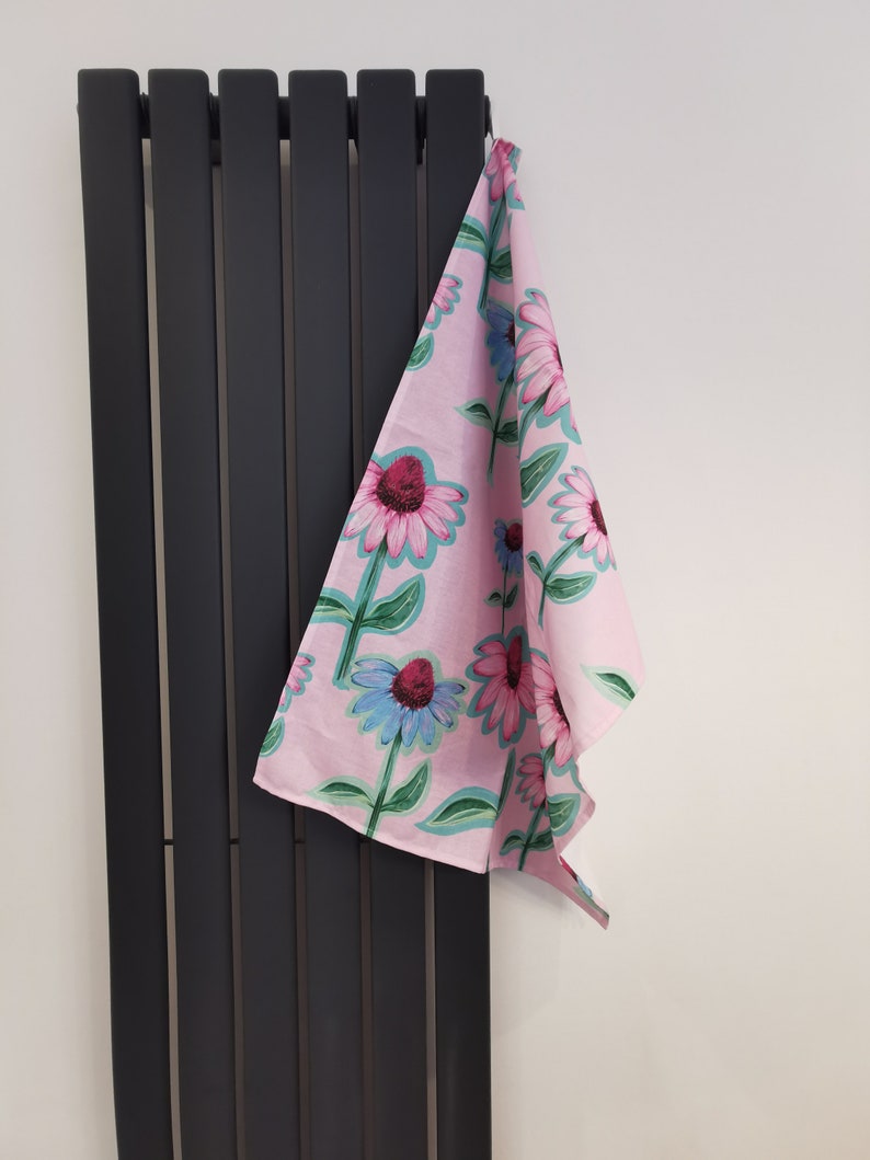 May include: A pink tea towel with a floral pattern of pink, blue, and green flowers. The towel is hanging on a black radiator.