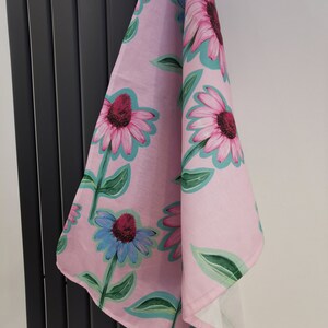 May include: A pink tea towel with a floral pattern of pink, blue, and green flowers. The flowers are stylized and have a whimsical look.