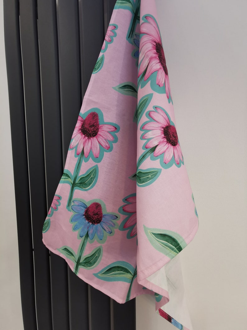 May include: A pink tea towel with a floral pattern of pink, blue, and green flowers. The flowers are stylized and have a whimsical look.