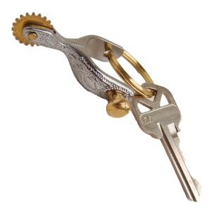 May include: A silver and gold metal key chain with a decorative spur design and a key with the number 56 on it.