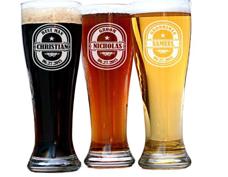 May include: Three tall beer glasses filled with different colored beers. Each glass has a personalized design with text. The first glass says "Best Man Christian 06.27.2015". The second glass says "Groom Nicholas 06.27.2015". The third glass says "Groomsman Samuel 06.27.2015".