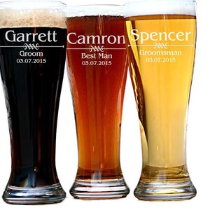 May include: Three tall beer glasses filled with different colored beers. Each glass is personalized with a name and role: Garrett, Groom; Camron, Best Man; and Spencer, Groomsman. The date 03.07.2015 is also printed on each glass.