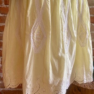 May include: A pale yellow cotton skirt with white lace trim and embroidery. The skirt has a scalloped hem and a gathered waist.