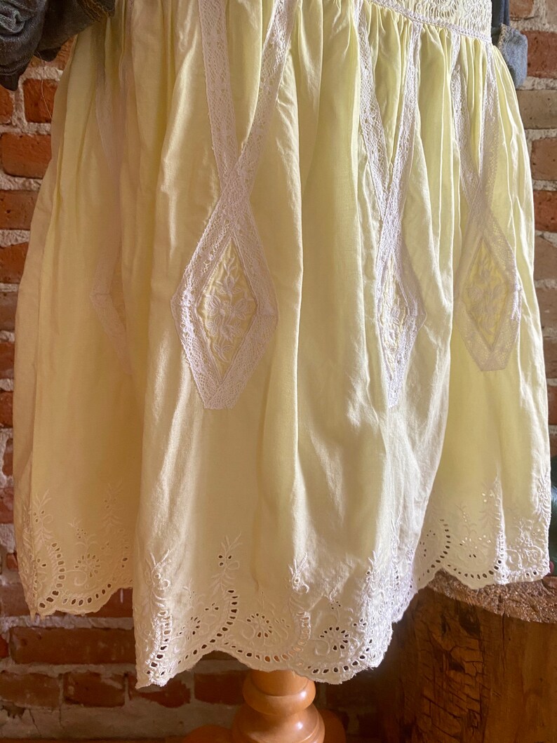 May include: A pale yellow cotton skirt with white lace trim and embroidery. The skirt has a scalloped hem and a gathered waist.