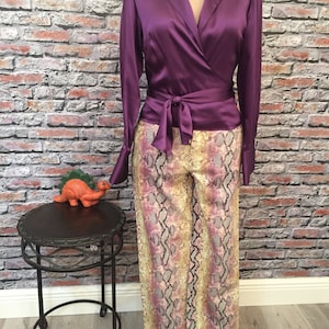 May include: A purple satin wrap blouse with long sleeves and a tie at the waist, paired with snakeskin print pants.