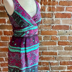 Peut inclure: Une robe sans manches avec un d&eacute;collet&eacute; en V et un motif g&eacute;om&eacute;trique color&eacute; dans les tons rose, violet, turquoise et noir. La robe a un corsage ajust&eacute; et une jupe fluide.