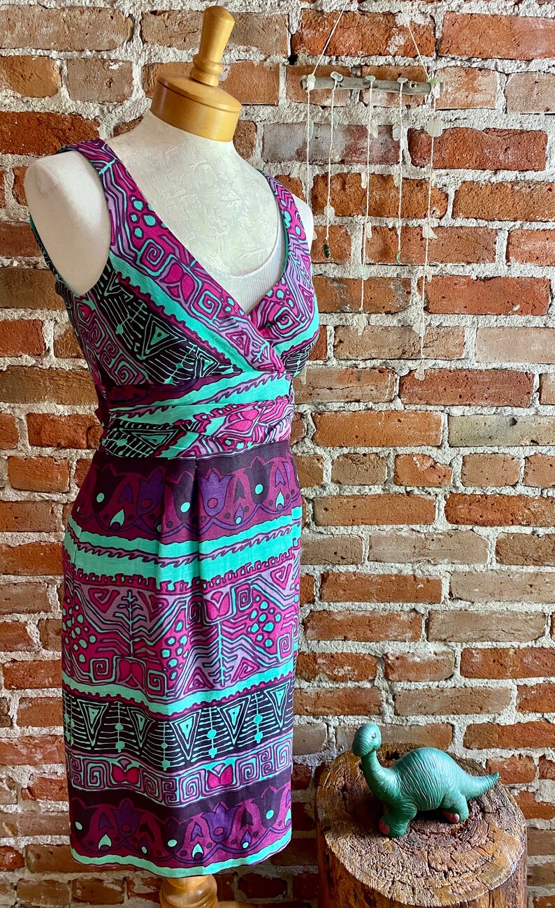 Peut inclure: Une robe sans manches avec un d&eacute;collet&eacute; en V et un motif g&eacute;om&eacute;trique color&eacute; dans les tons rose, violet, turquoise et noir. La robe a un corsage ajust&eacute; et une jupe fluide.