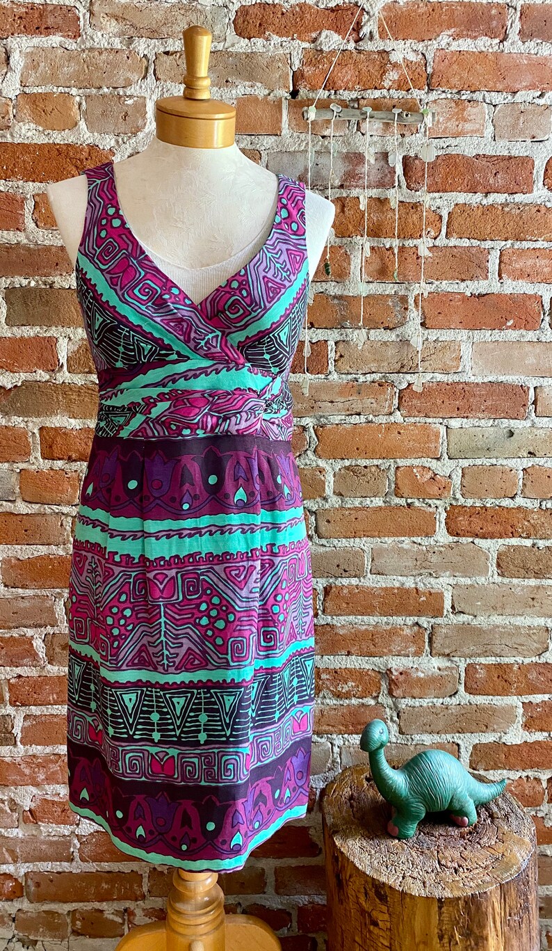 Peut inclure: Une robe sans manches avec un d&eacute;collet&eacute; en V et un motif g&eacute;om&eacute;trique color&eacute; dans des tons de rose, violet, vert et marron. La robe a un corsage ajust&eacute; et une jupe fluide.
