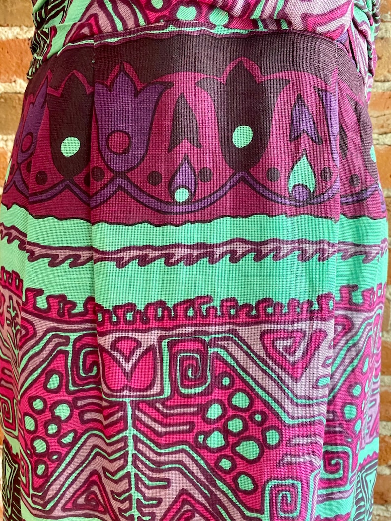 Peut inclure: Gros plan sur une jupe avec un motif g&eacute;om&eacute;trique color&eacute;. La jupe est en tissu tiss&eacute; et pr&eacute;sente une palette de couleurs rose, verte et violette.