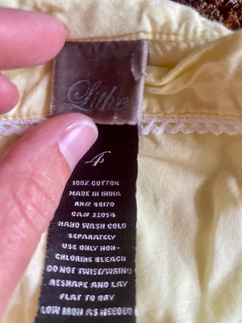 May include: A black and white care label for a garment made of 100% cotton. The label includes instructions for hand washing cold, using only non-chlorine bleach, and laying flat to dry. The label also includes the text "Made in India", "RN# 66170", and "CA# 3205/4".
