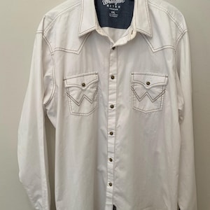 May include: White Wrangler Retro shirt with brown stitching and two chest pockets. The shirt has a button-down front and cuffs, and the Wrangler logo is visible on the collar. The shirt is a size XXL.