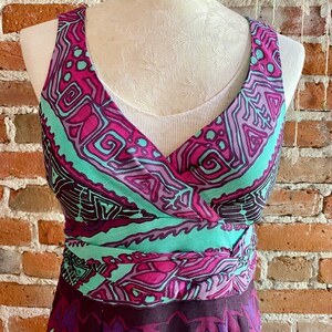 Peut inclure: Une robe sans manches avec un d&eacute;collet&eacute; en V et un motif g&eacute;om&eacute;trique color&eacute; dans les tons rose, violet, vert et noir. La robe a une ceinture &agrave; nouer &agrave; la taille et une jupe fluide.
